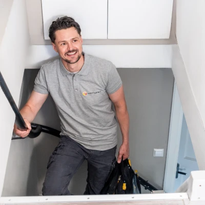 Instalalteur met grijs t-shirt met het logo van Warmgarant komt de trap op