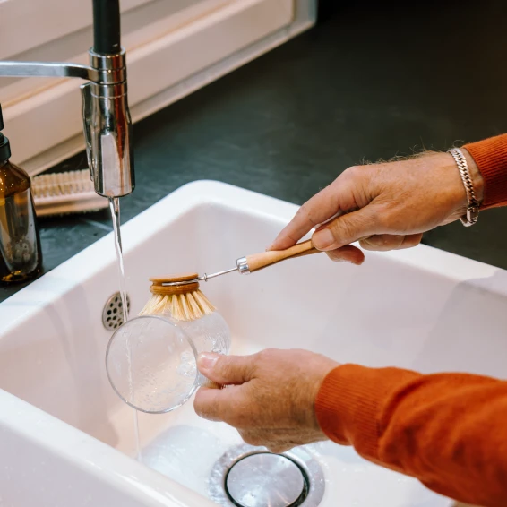 Op de foto is een man een theekop aan het afwassen, er komt warm water uit de kraan.