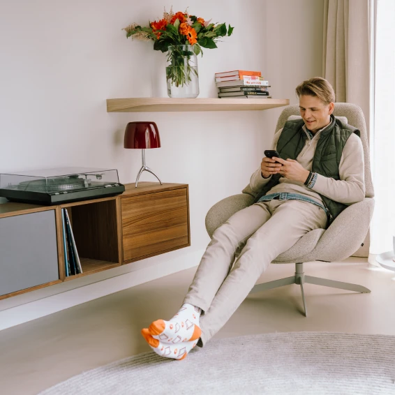 Man zit ontspannen op een fauteuil in de woonkamer op zijn telefoon.