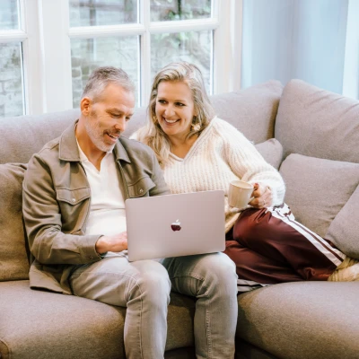 Stel zit op de bank met een laptop op schoot.