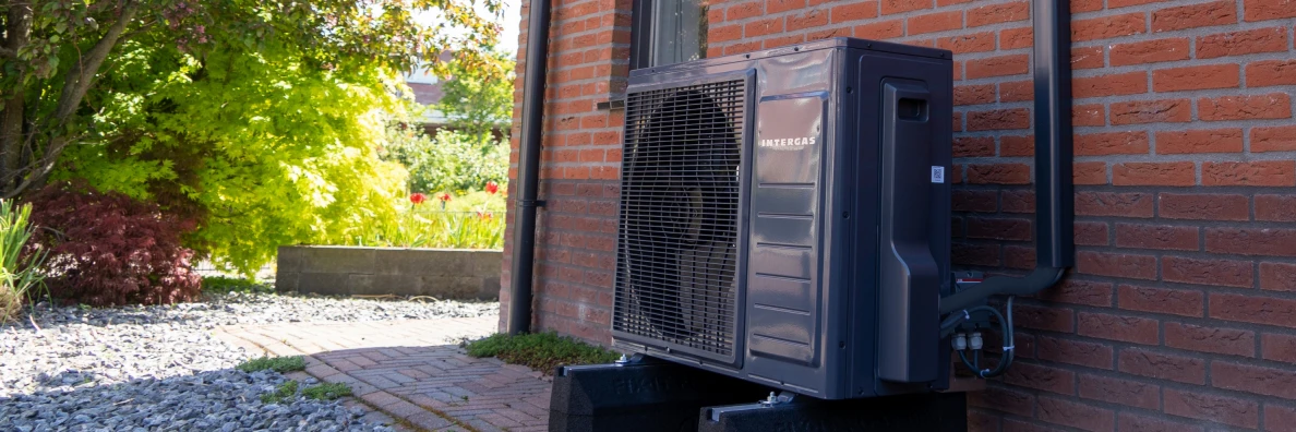 Intergas warmtepomp staat naast een huis buiten in de tuin.