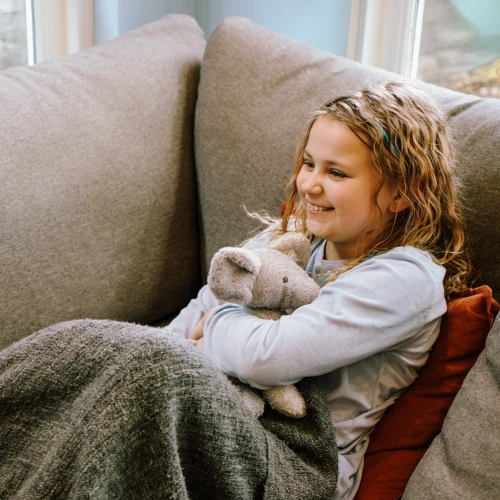 Meisje ligt op de bank met een dekentje om en een knuffel van een muis in haar armen.