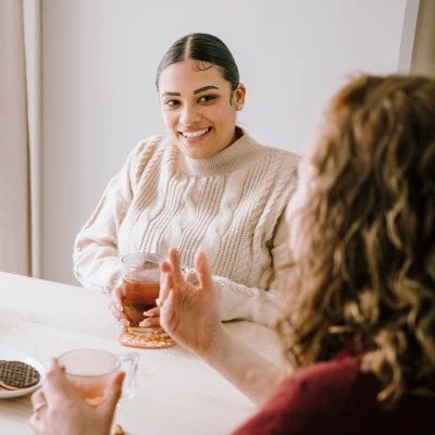 Op de foto zitten twee vrouwen aan tafel thee te drinken en te praten