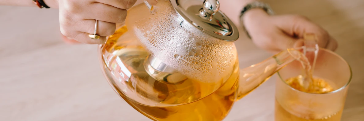 Op de foto zie je een jonge vrouw rooibos thee inschenken uit een glazen theekan.